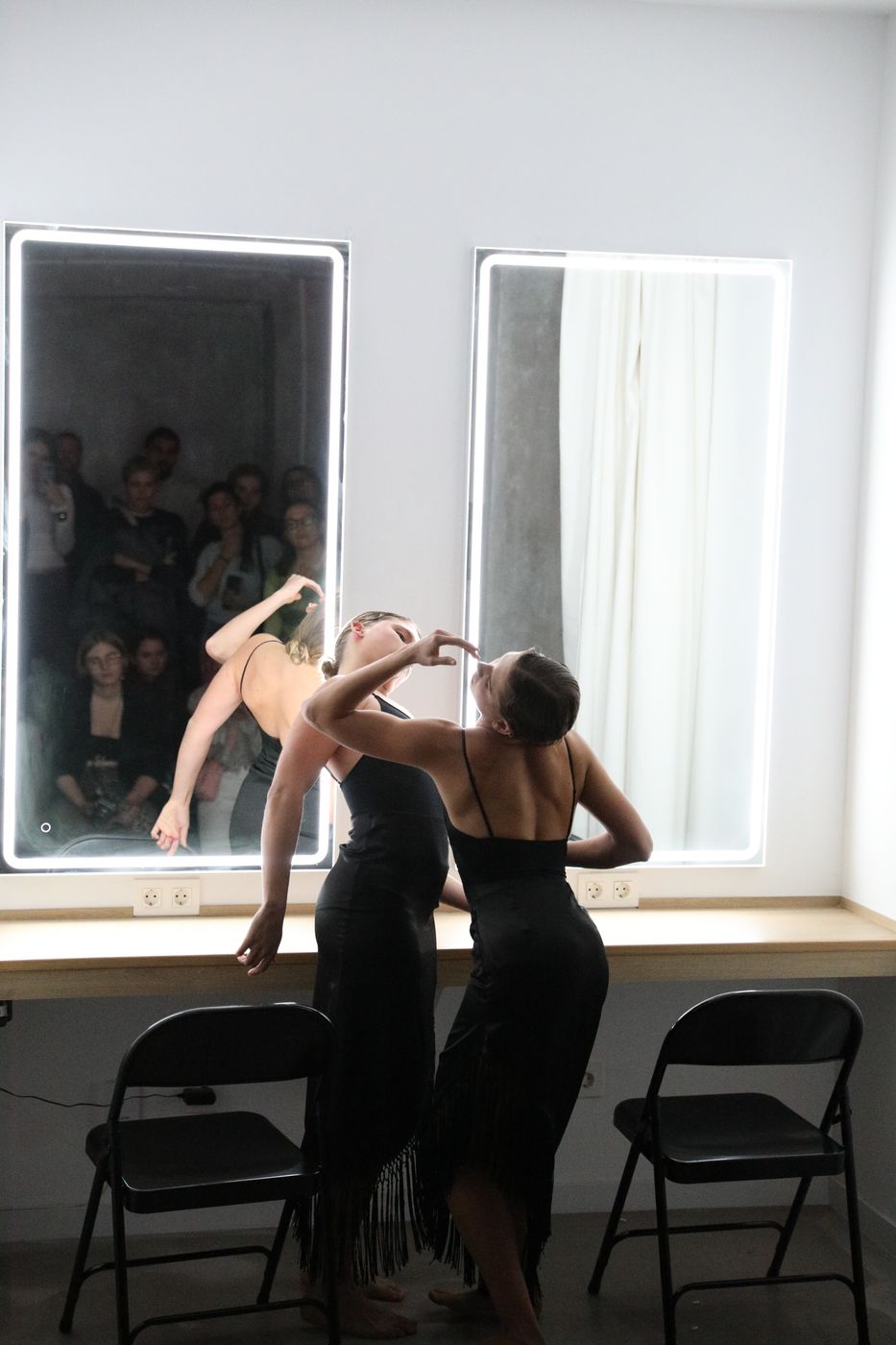 Two dancers in black lean back in front of a lit mirror at Només aquí