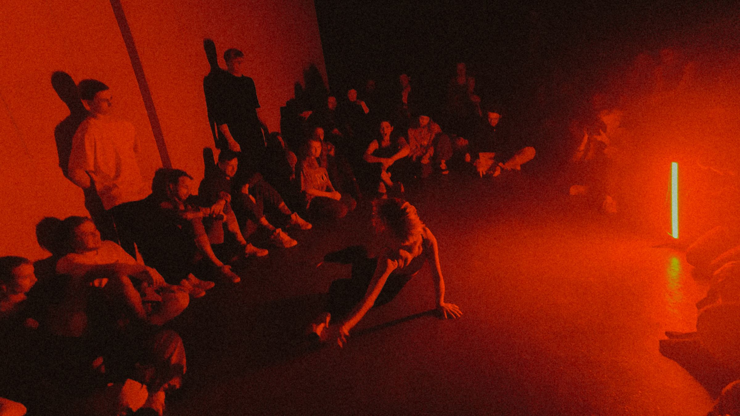 Dancers watch a performer on a red-lit floor at One Light Jam