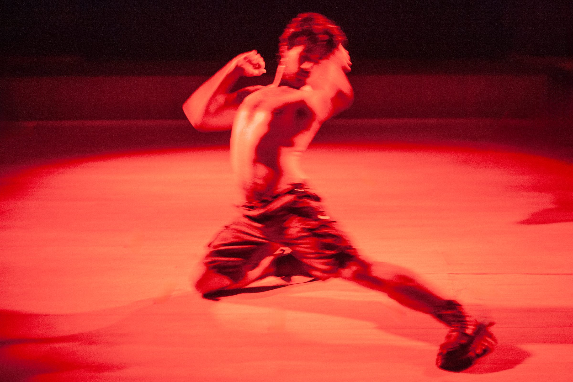 A performer leaps across a red-lit floor in PICME
