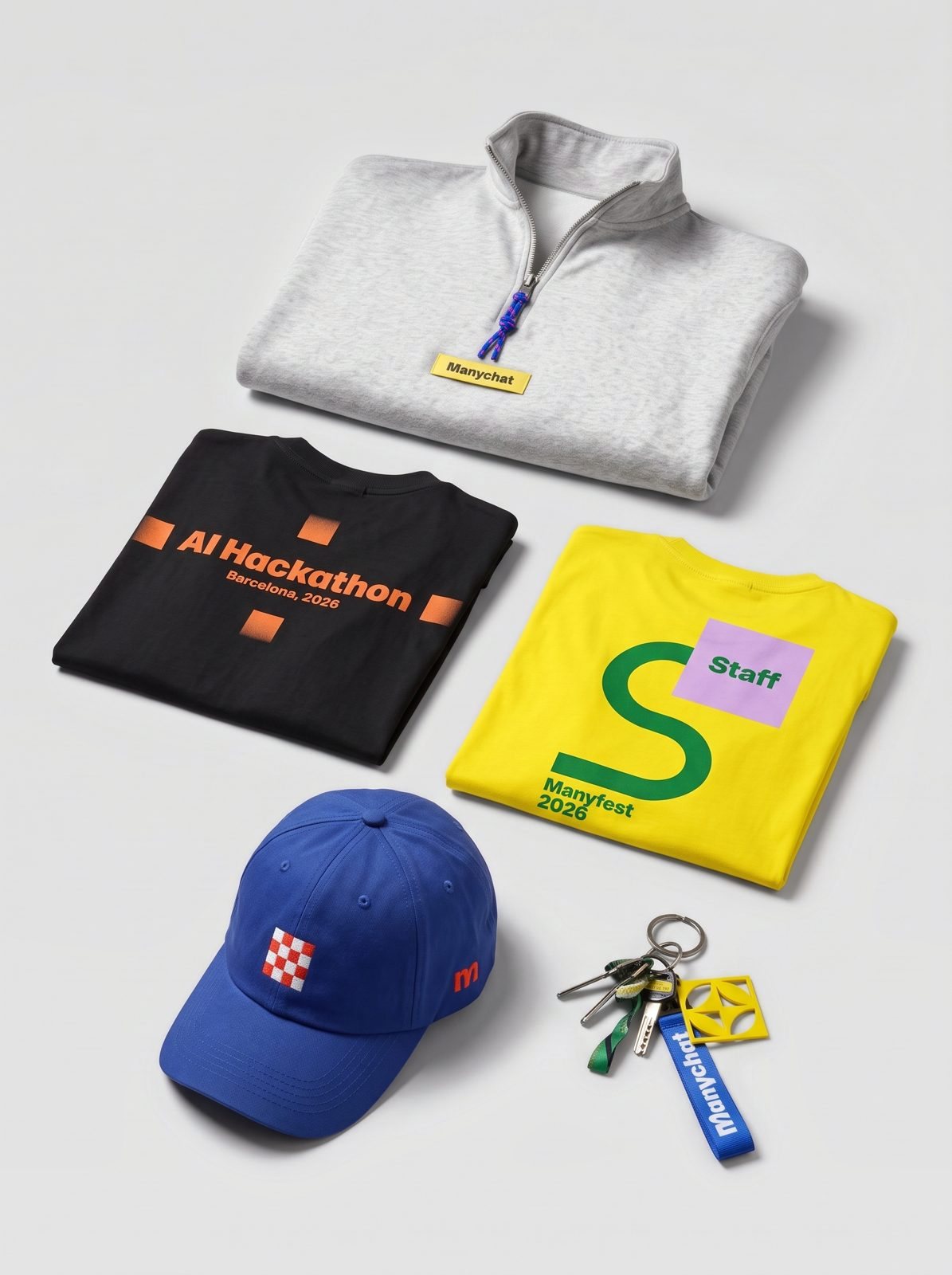 The whole Manyfest edition laid out in the studio: quarter-zip, two T-shirts, cap and keychain