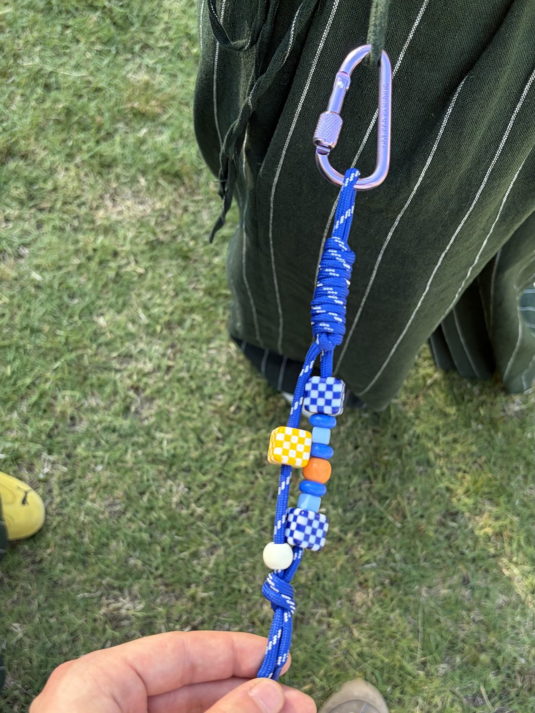 A blue cord keychain with checker beads and a carabiner, held up on the festival lawn
