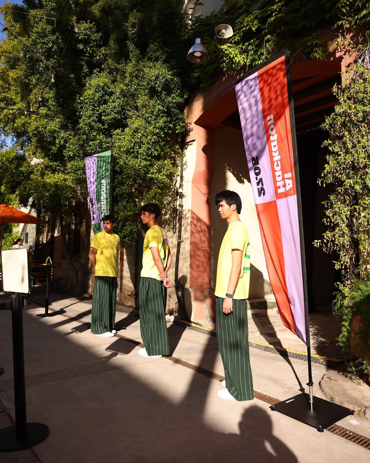 Three crew members in yellow T-shirts by the festival flags, the back print visible