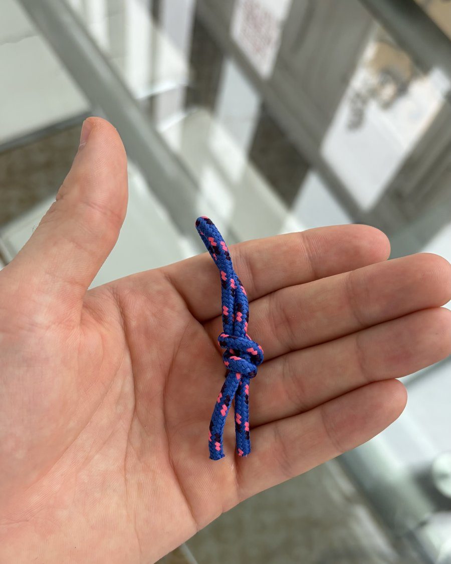 A blue paracord zip pull with a knot, held in an open hand