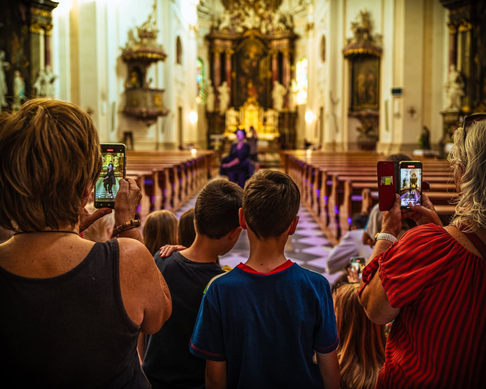 Children and parents in the aisle of a baroque church filming a dancer at the altar