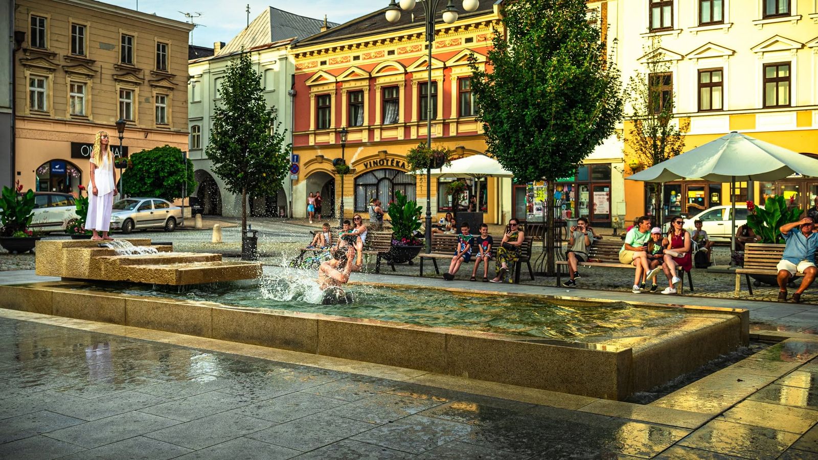 Dancers in white by the fountain on the town square, guests at the café tables around it