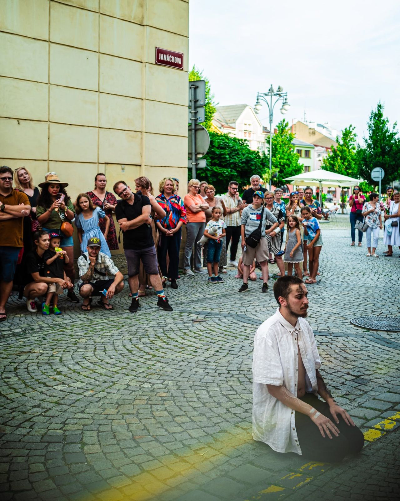 A performer kneeling on the cobbles in front of a crowd of guests, a yellow line painted on the street