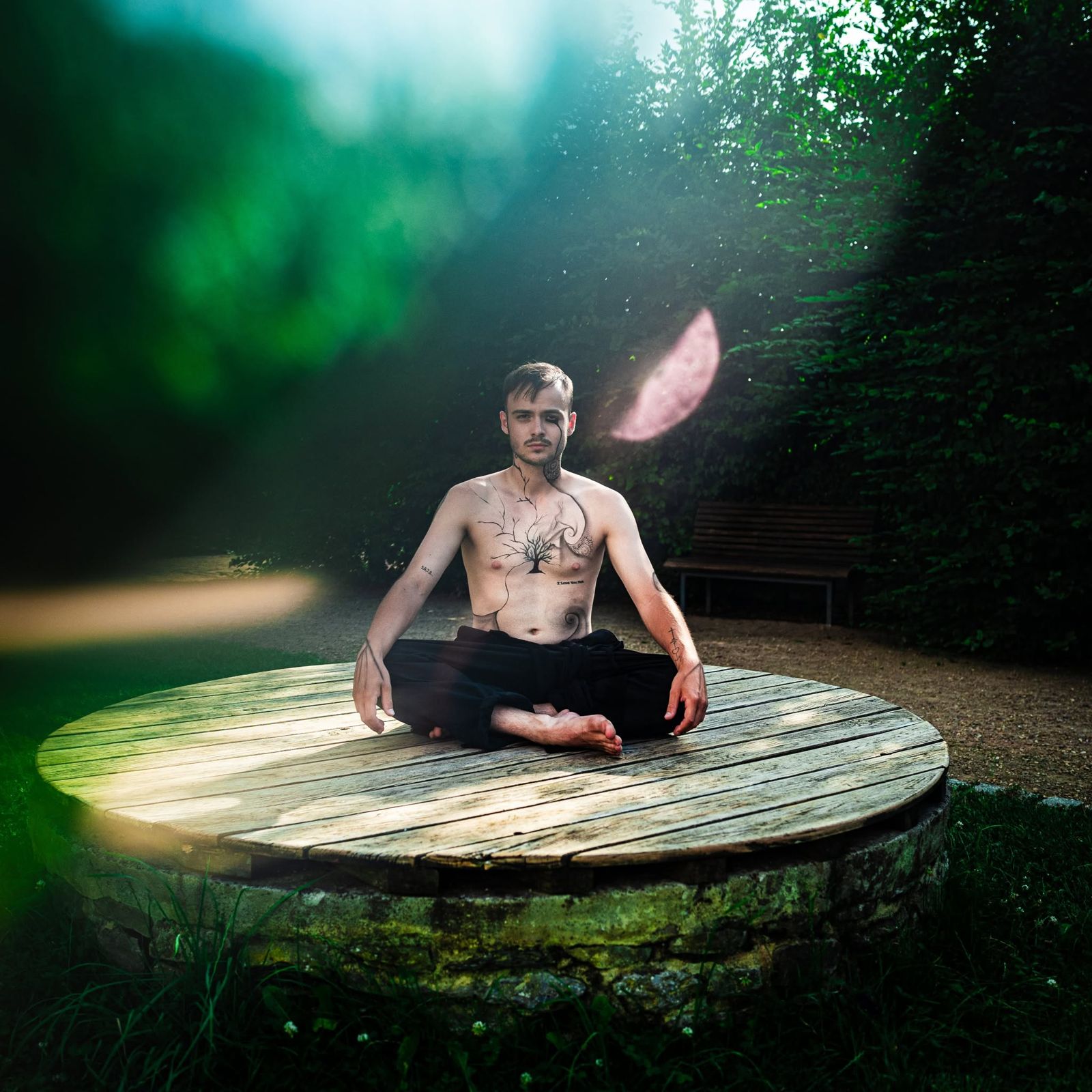 A performer sitting cross-legged on a round wooden platform in a dark green garden