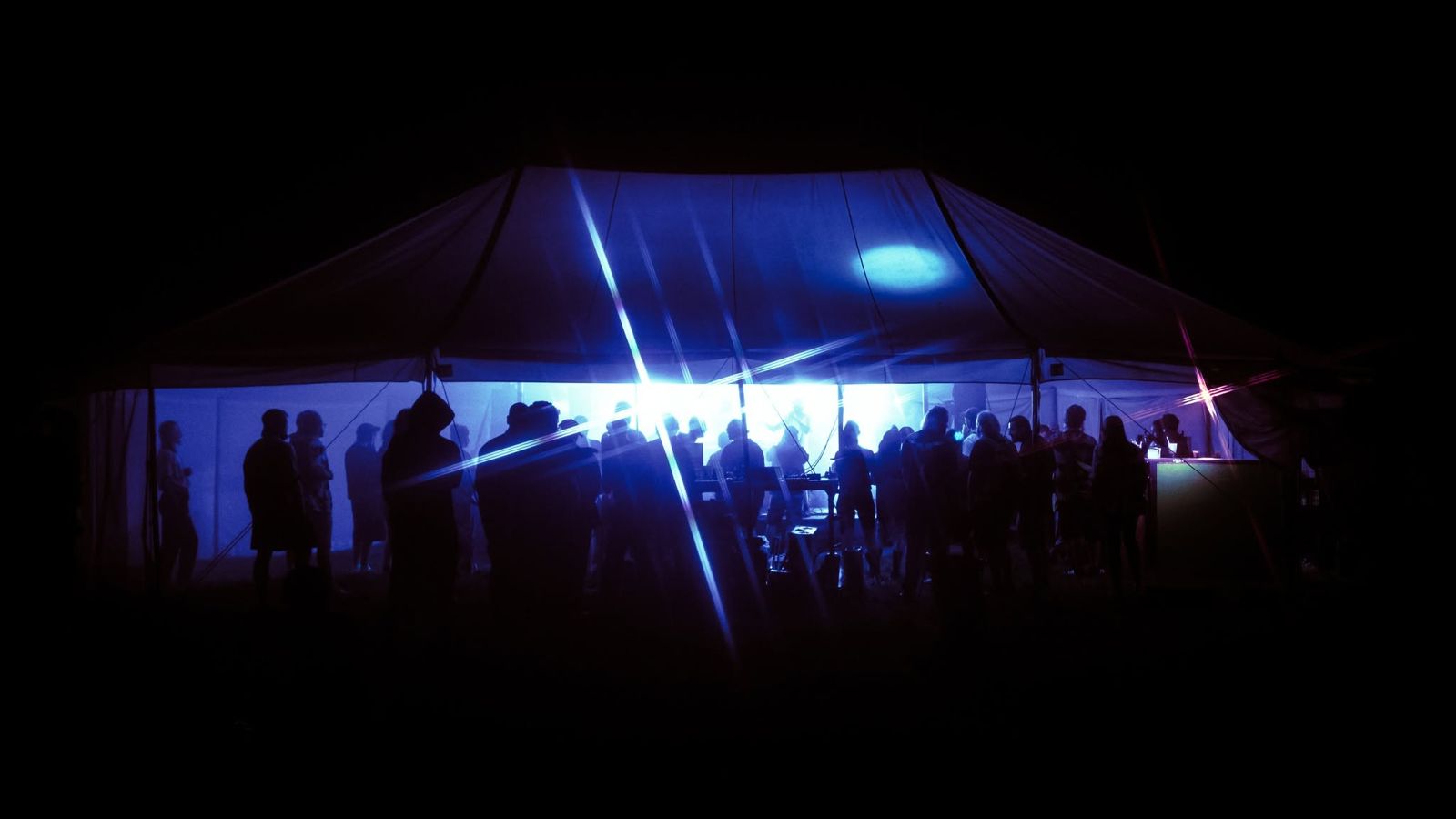 The rave tent at night, blue light beams over the dancing crowd