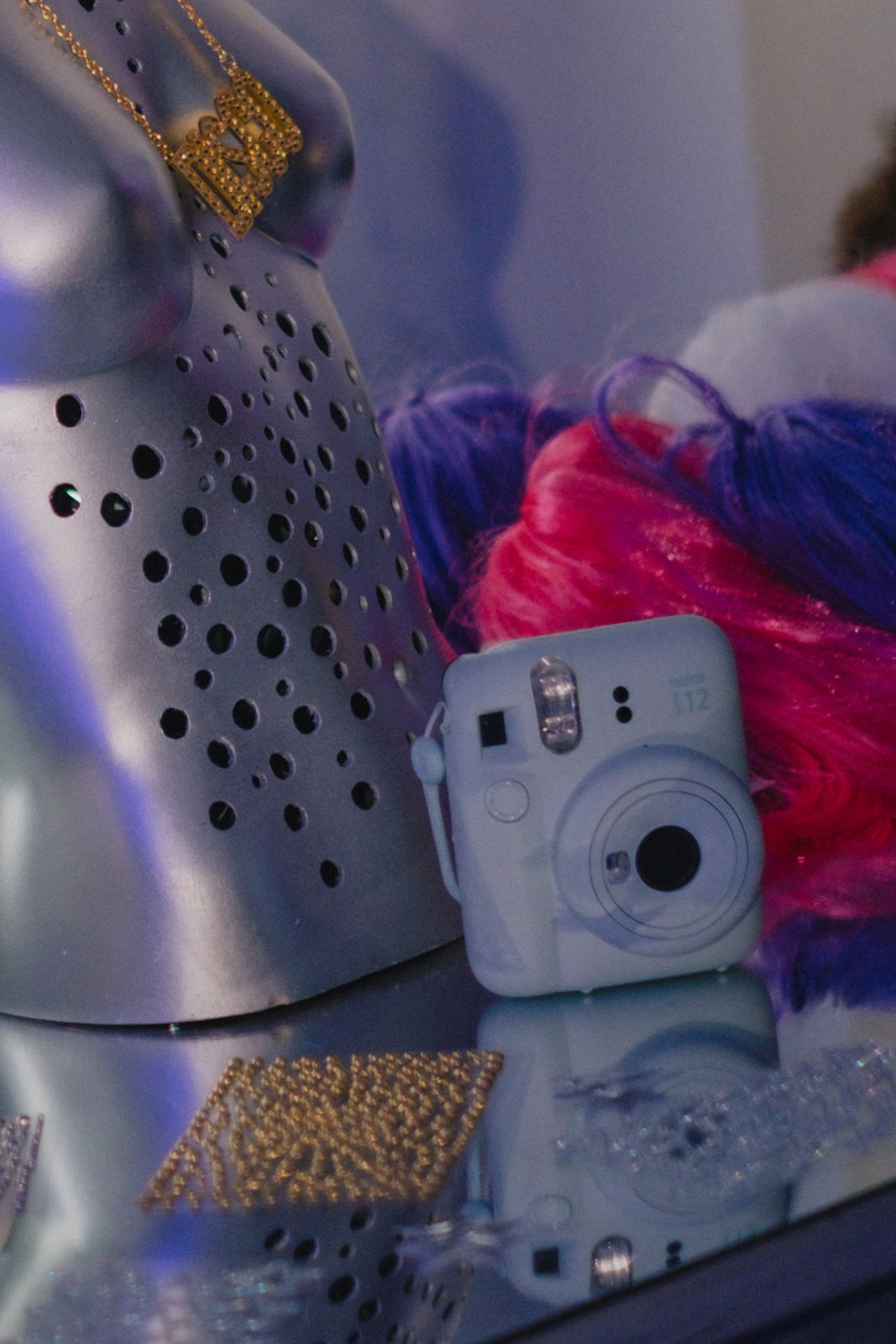 An instant camera among silver mannequins and face gems
