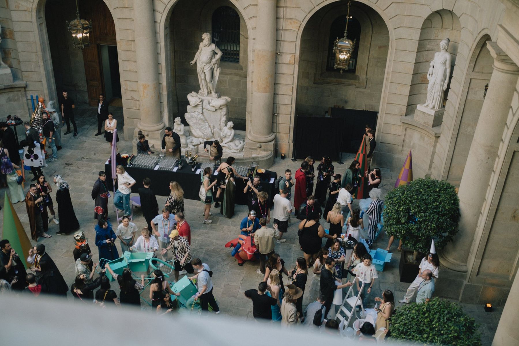 The courtyard of the Academy of Fine Arts from above, full of guests in costume between striped cones and statues