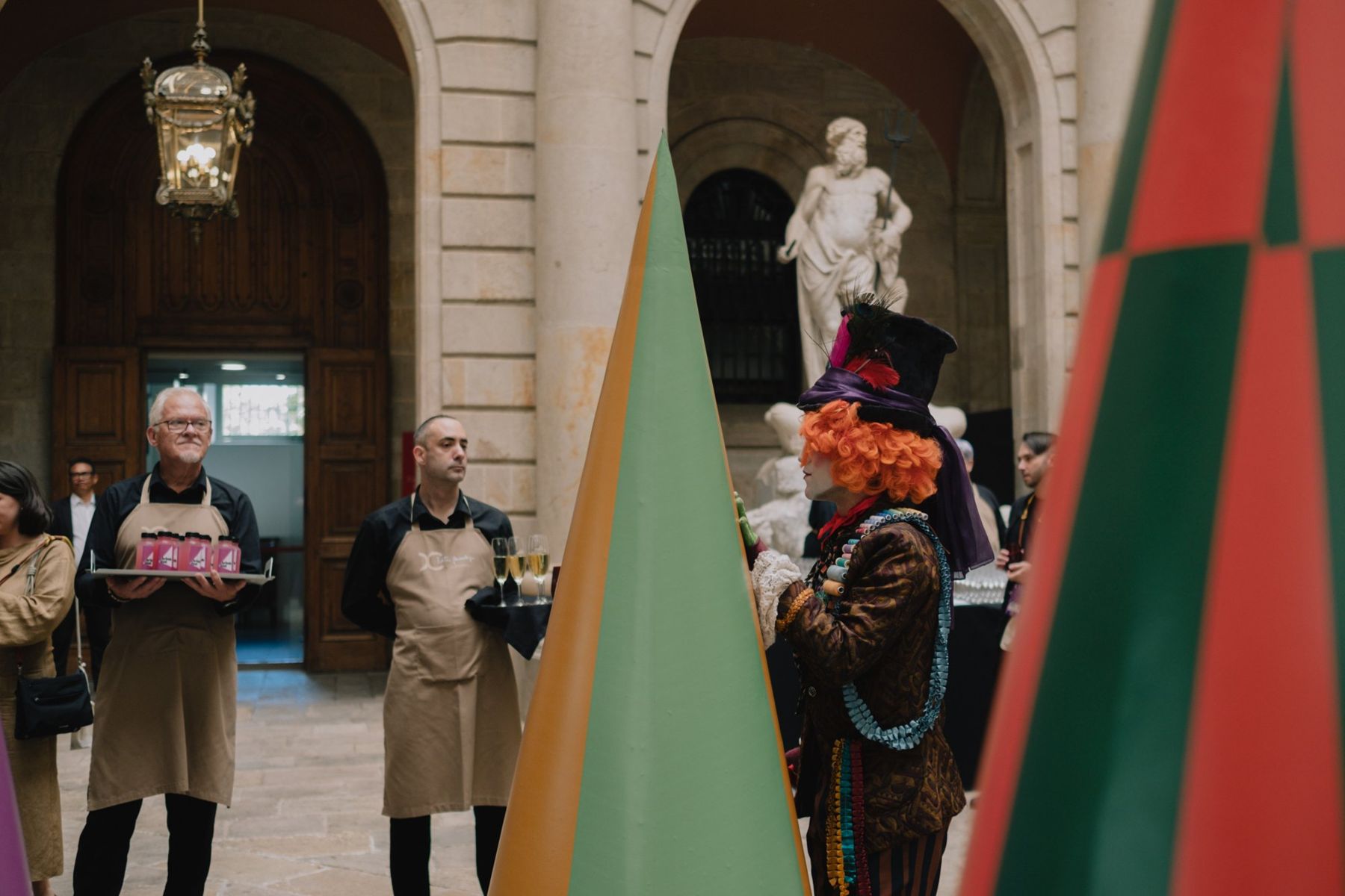 Waiters with trays and a character in a top hat between tall green and red cones in the arcade