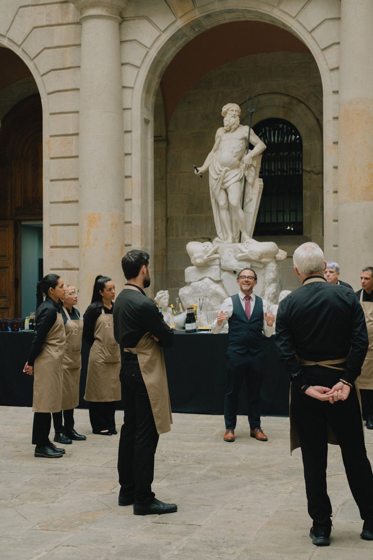The service team in aprons at a briefing in the courtyard, a marble statue behind them