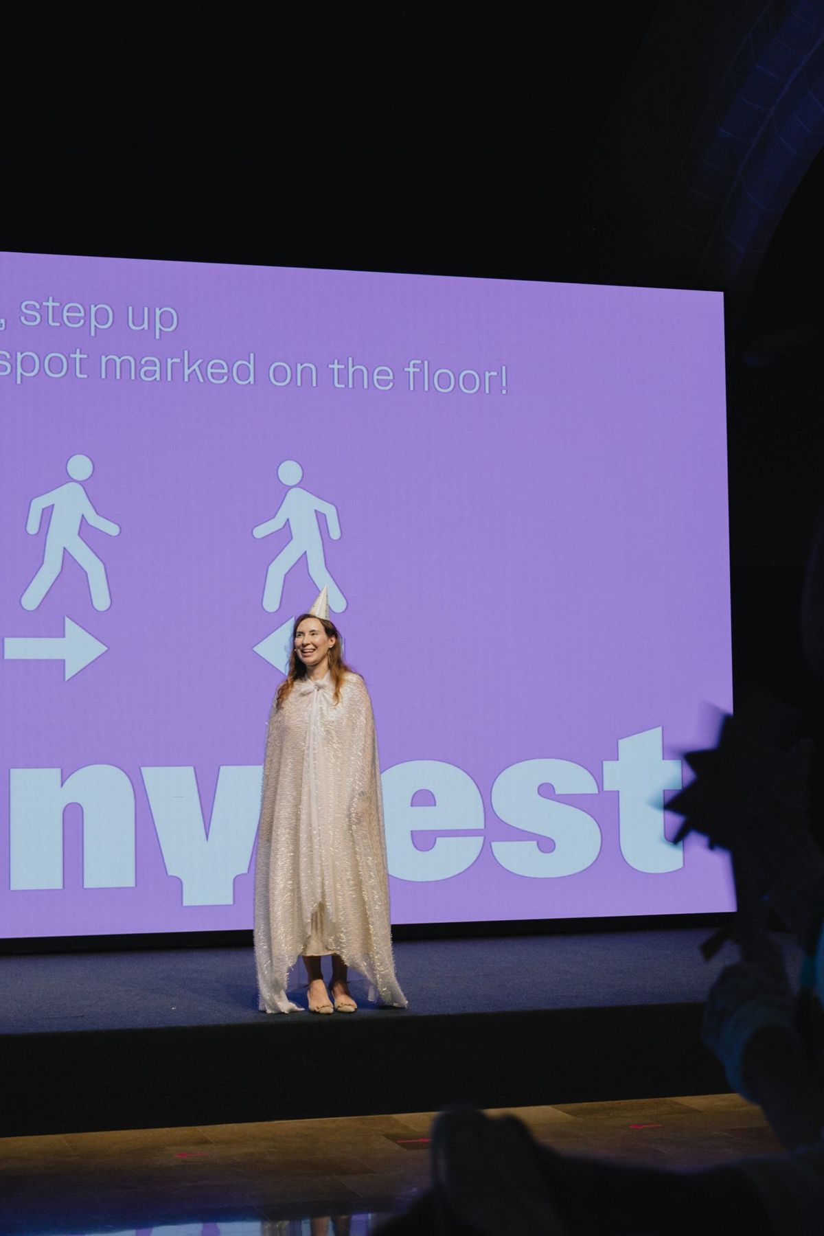 The host on stage in a long cape in front of the Manyfest screen