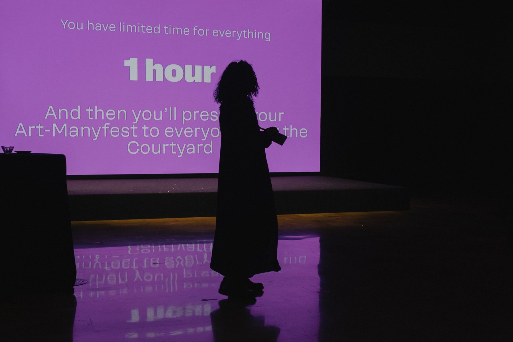 A silhouette on stage in front of a purple slide giving the time left