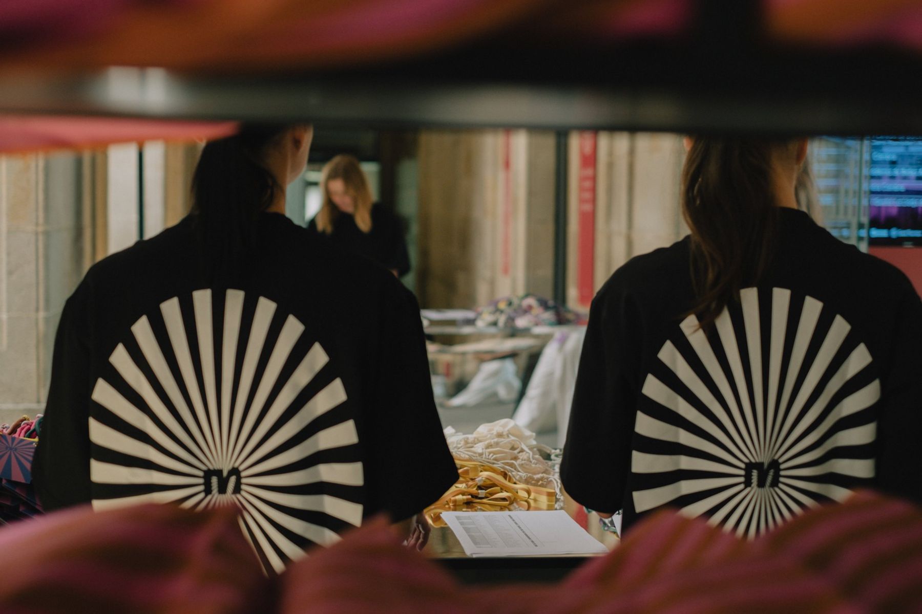 Two crew members from behind, each with a white sunburst printed on the back of a black tee