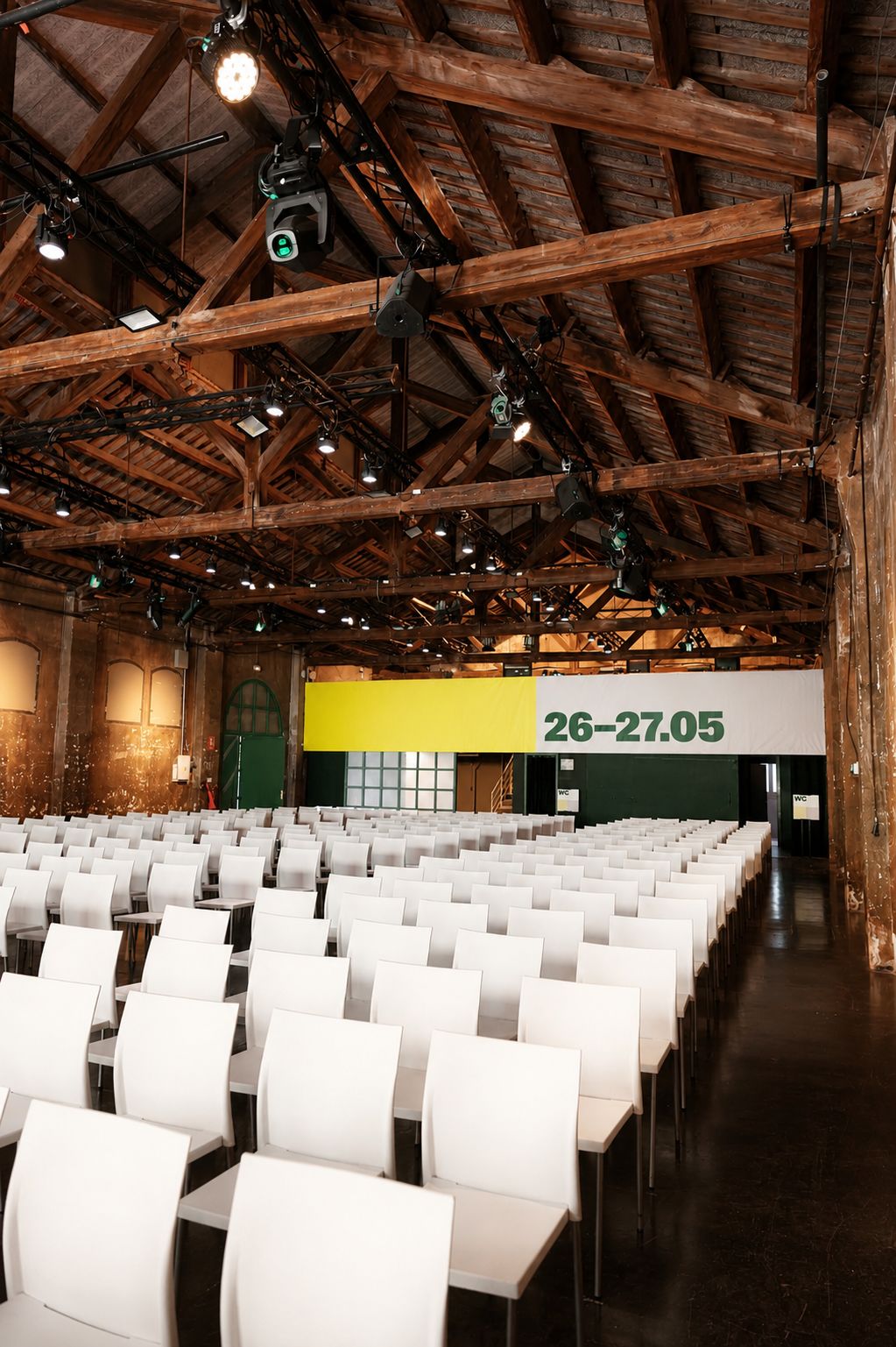 Rows of white chairs in a brick hall facing a yellow stage