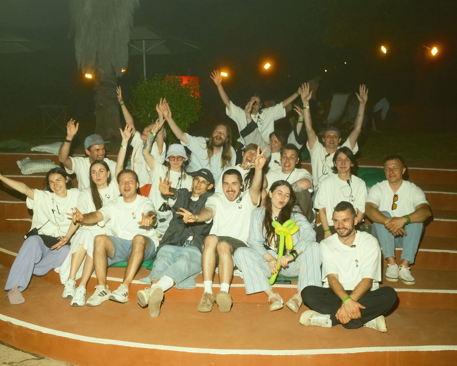 The festival team in white T-shirts sitting together on the terrace steps at night