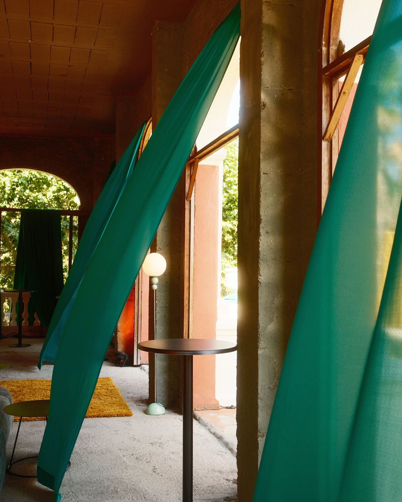 Green curtains blowing in an arched gallery with a sofa