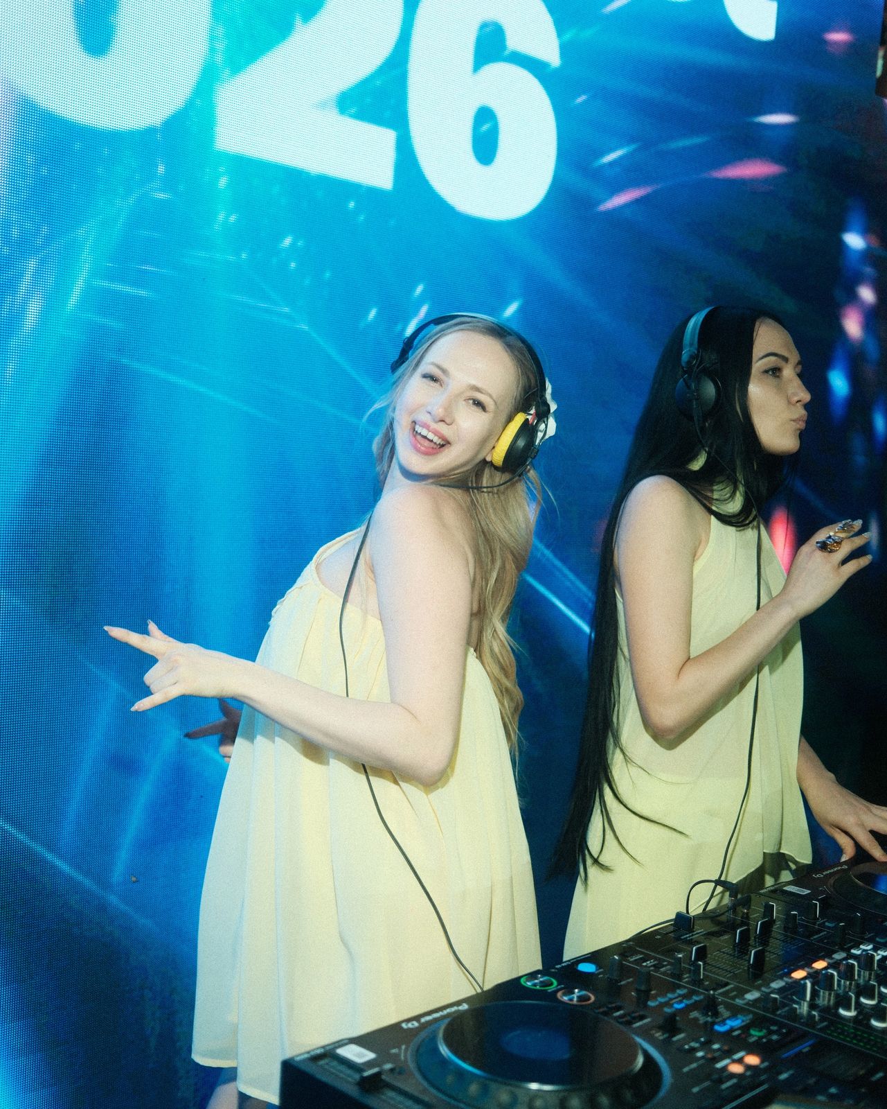Two DJs in yellow dresses dancing behind the decks