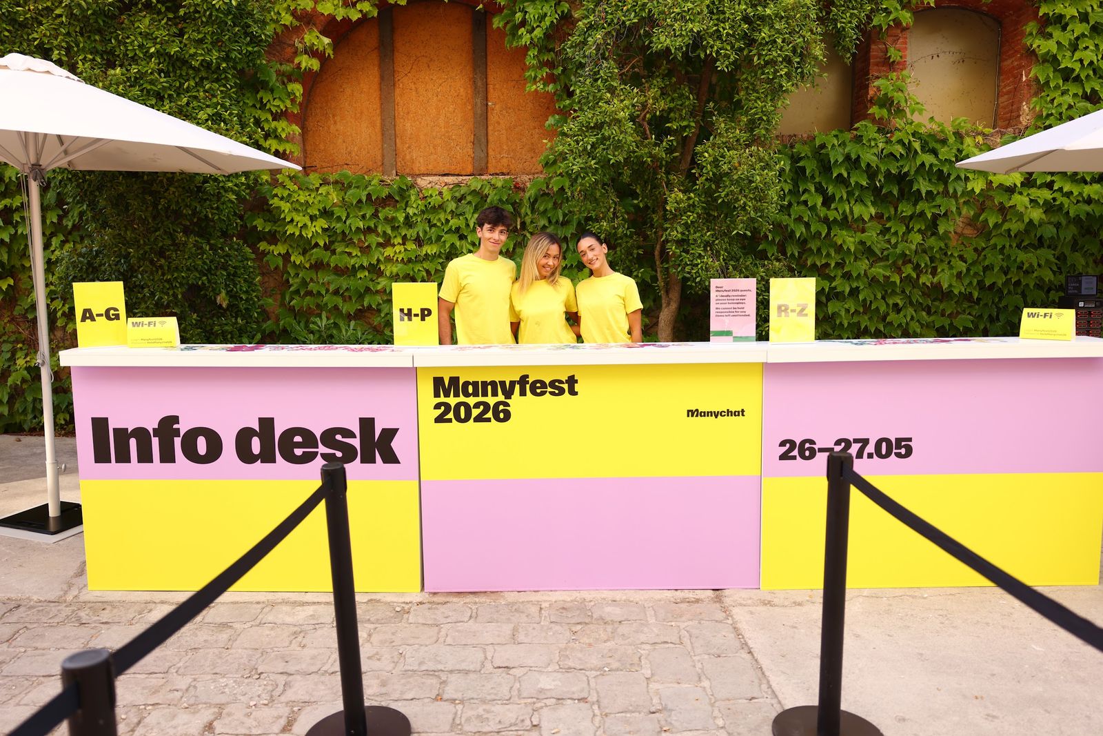 The info desk team in yellow T-shirts behind a yellow and pink Manyfest 2026 desk