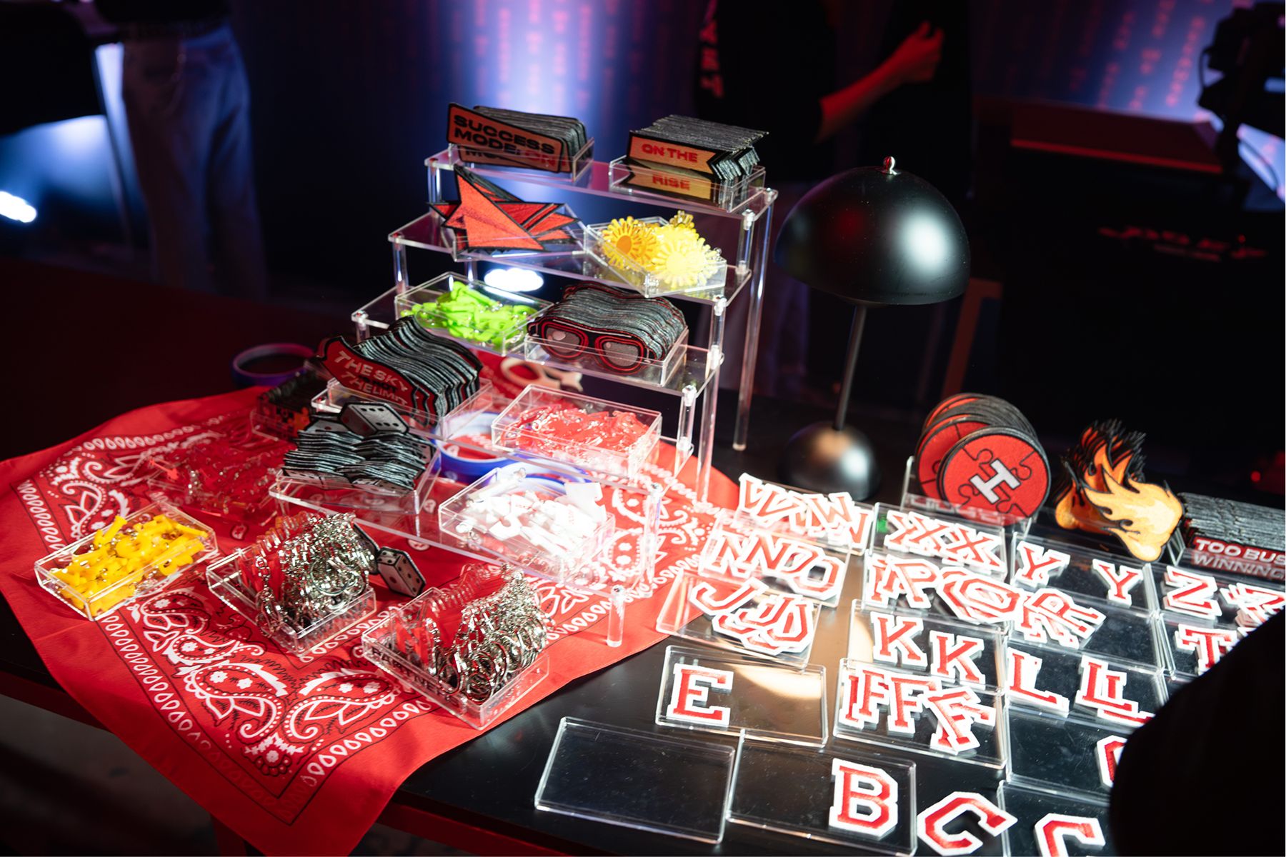 The Patch Bar table: acrylic trays of patches and varsity letters on red bandanas