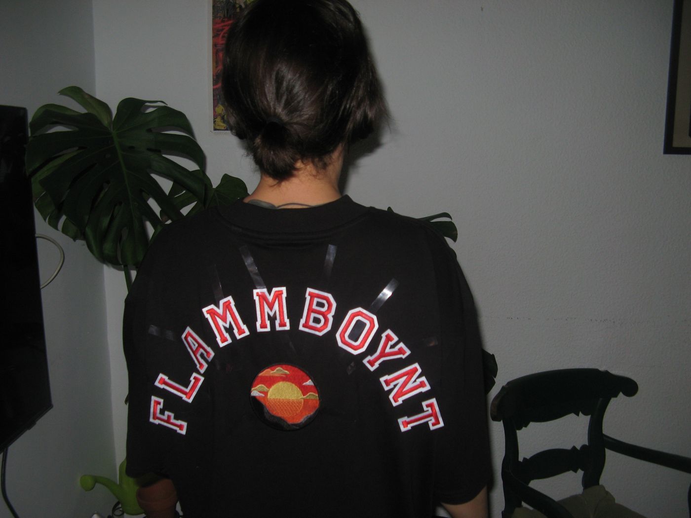 The back of a black tee lettered FLAMMBOYNT around a sunset patch