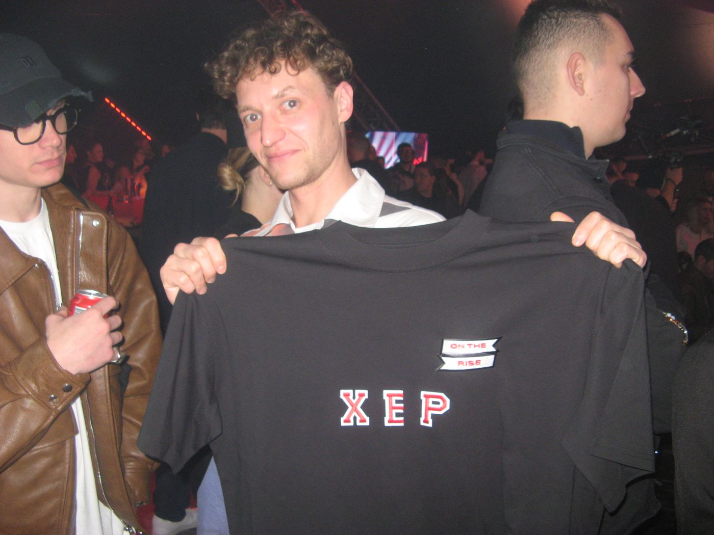 A guest holding up a black tee lettered XEP