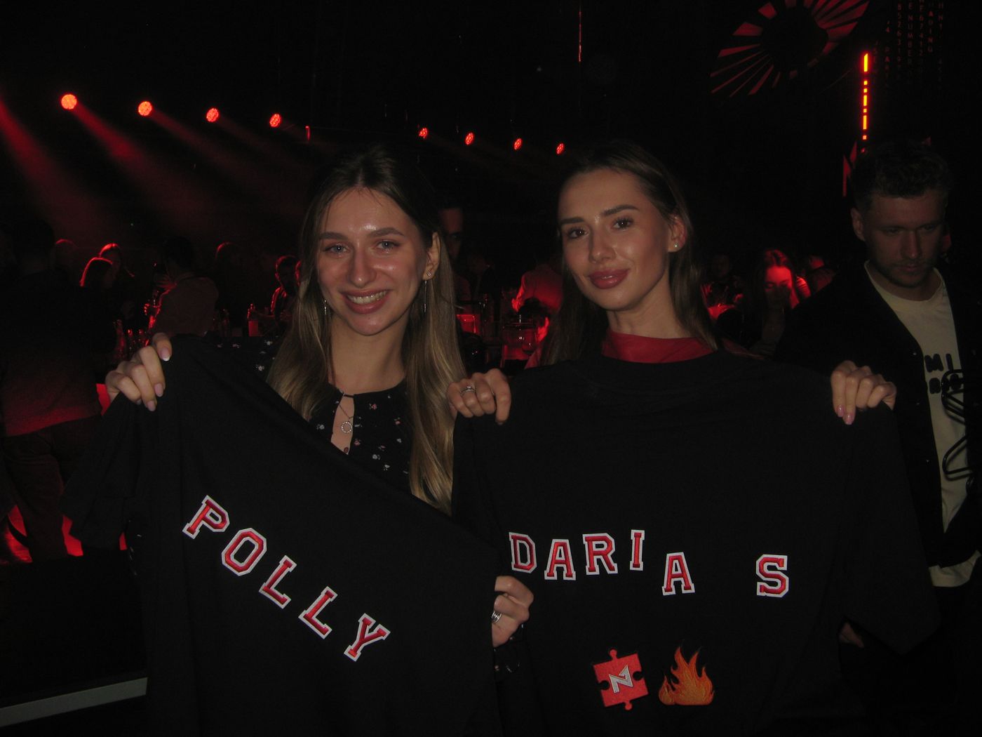 Two guests holding sweatshirts lettered POLLY and DARIA S