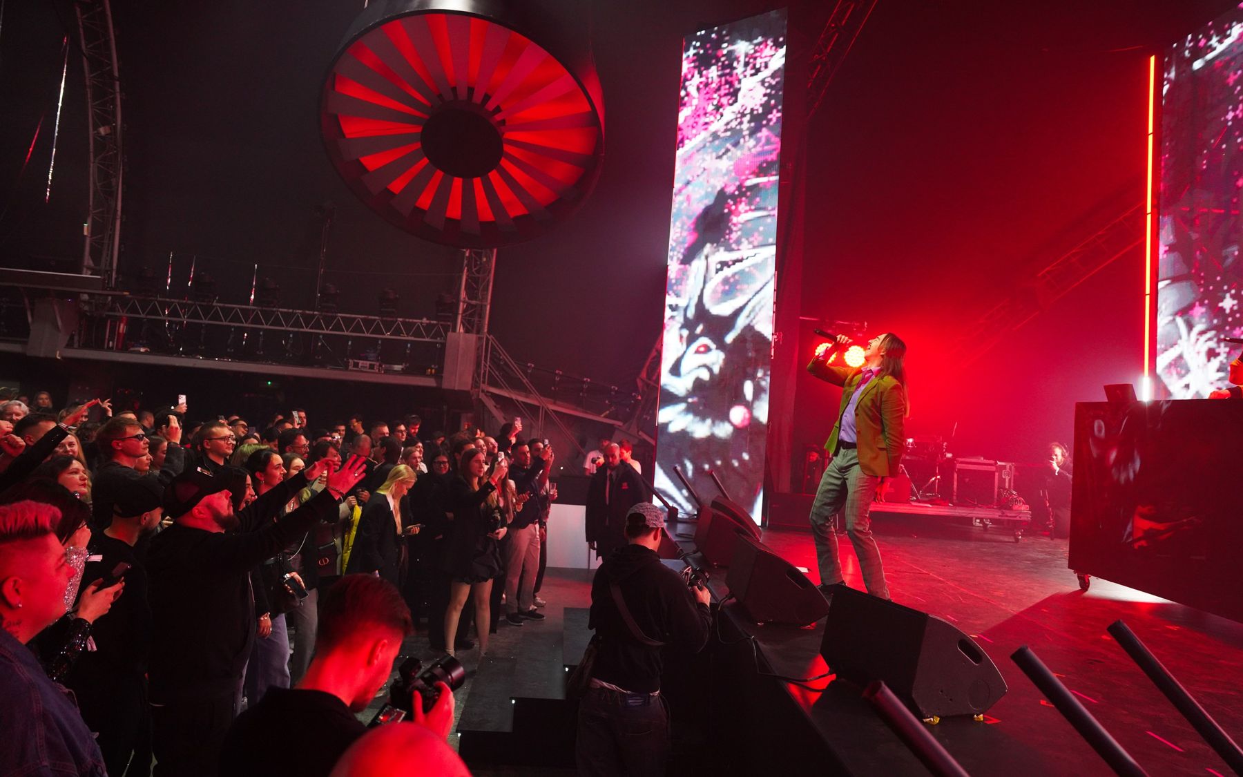 A singer on stage in front of the crowd and a red fan wall