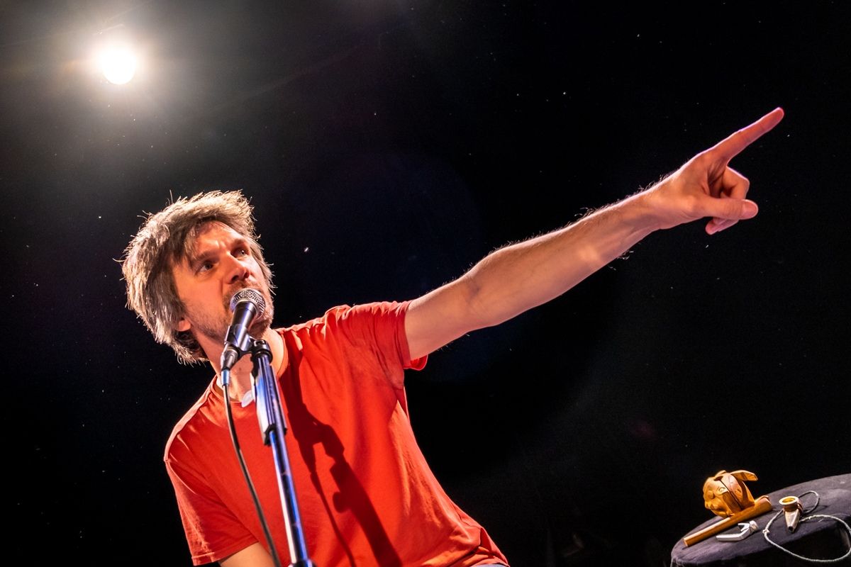 A singer in a red shirt pointing up into the stage light