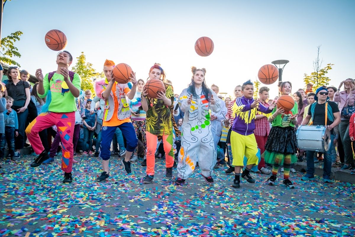 Young performers throwing basketballs high into the air on a confetti-covered street