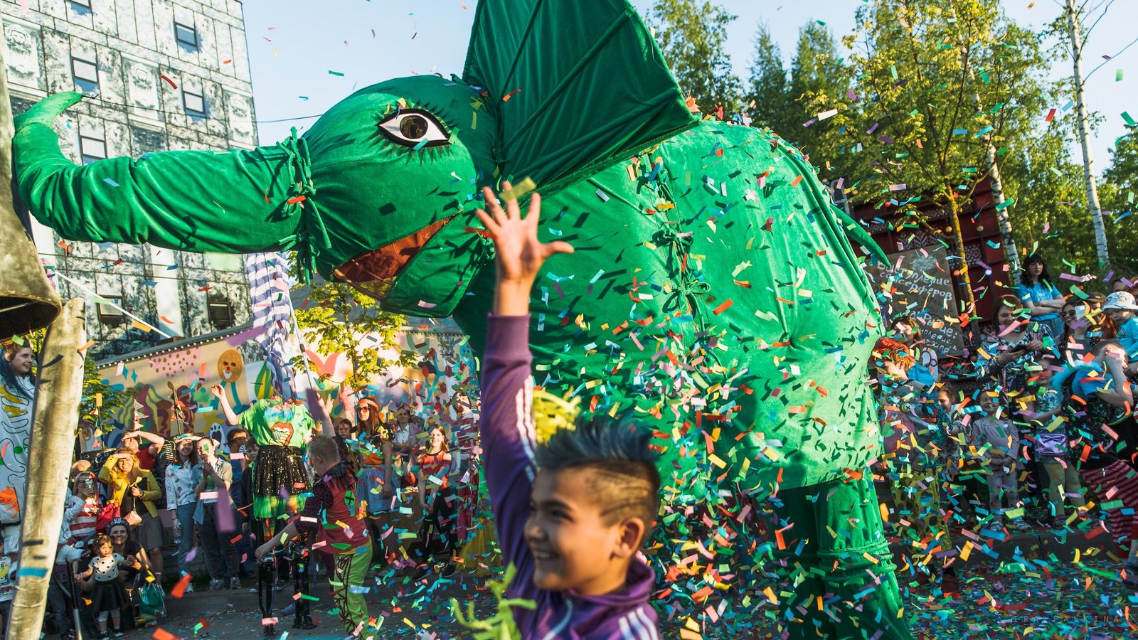 A giant green dragon puppet under a cloud of confetti