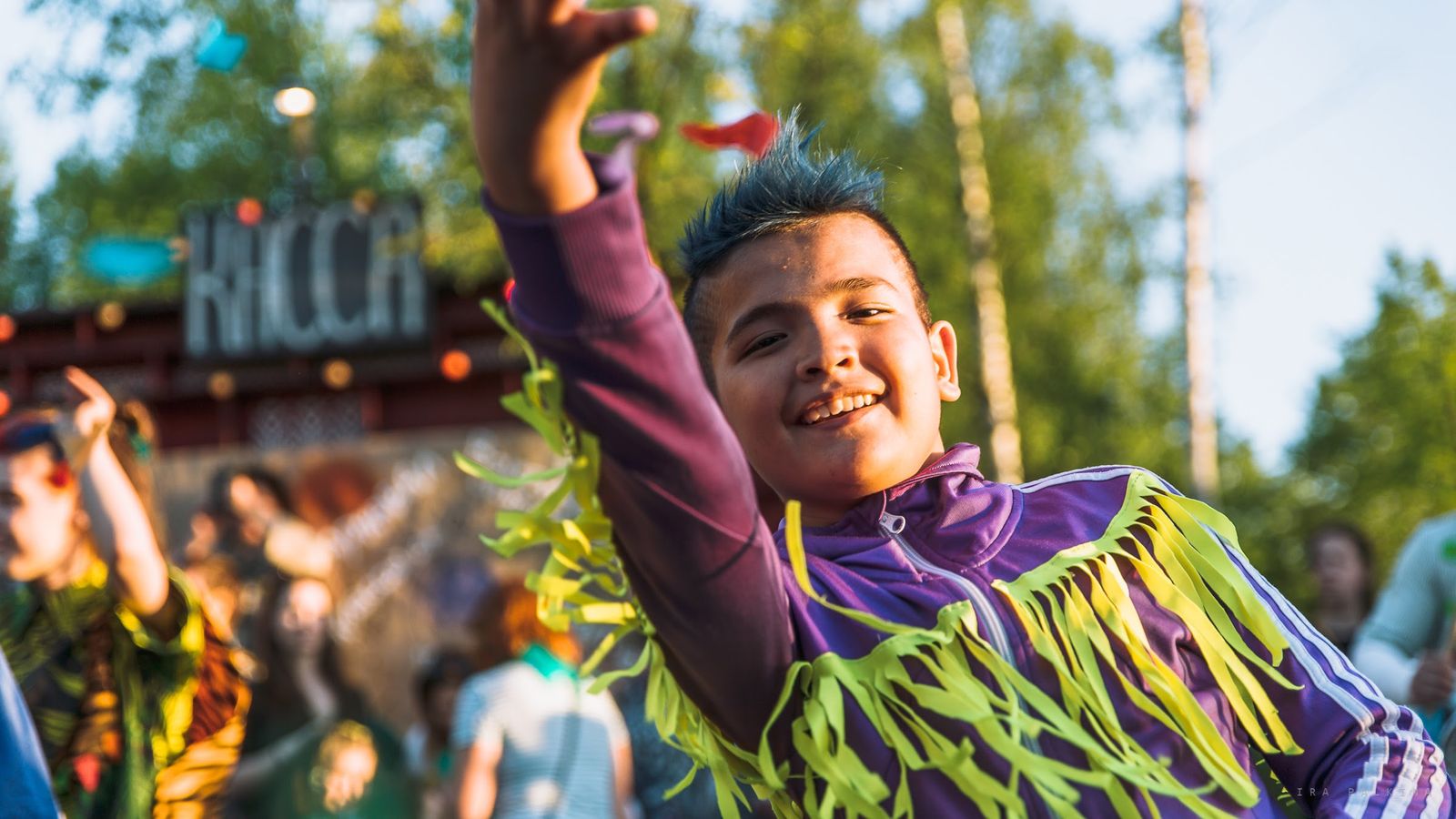 A young performer in a purple jacket with green fringe dancing with one arm raised
