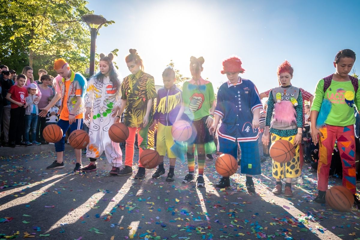 The carnival troupe lined up in costumes with drums and basketballs, backlit by the sun