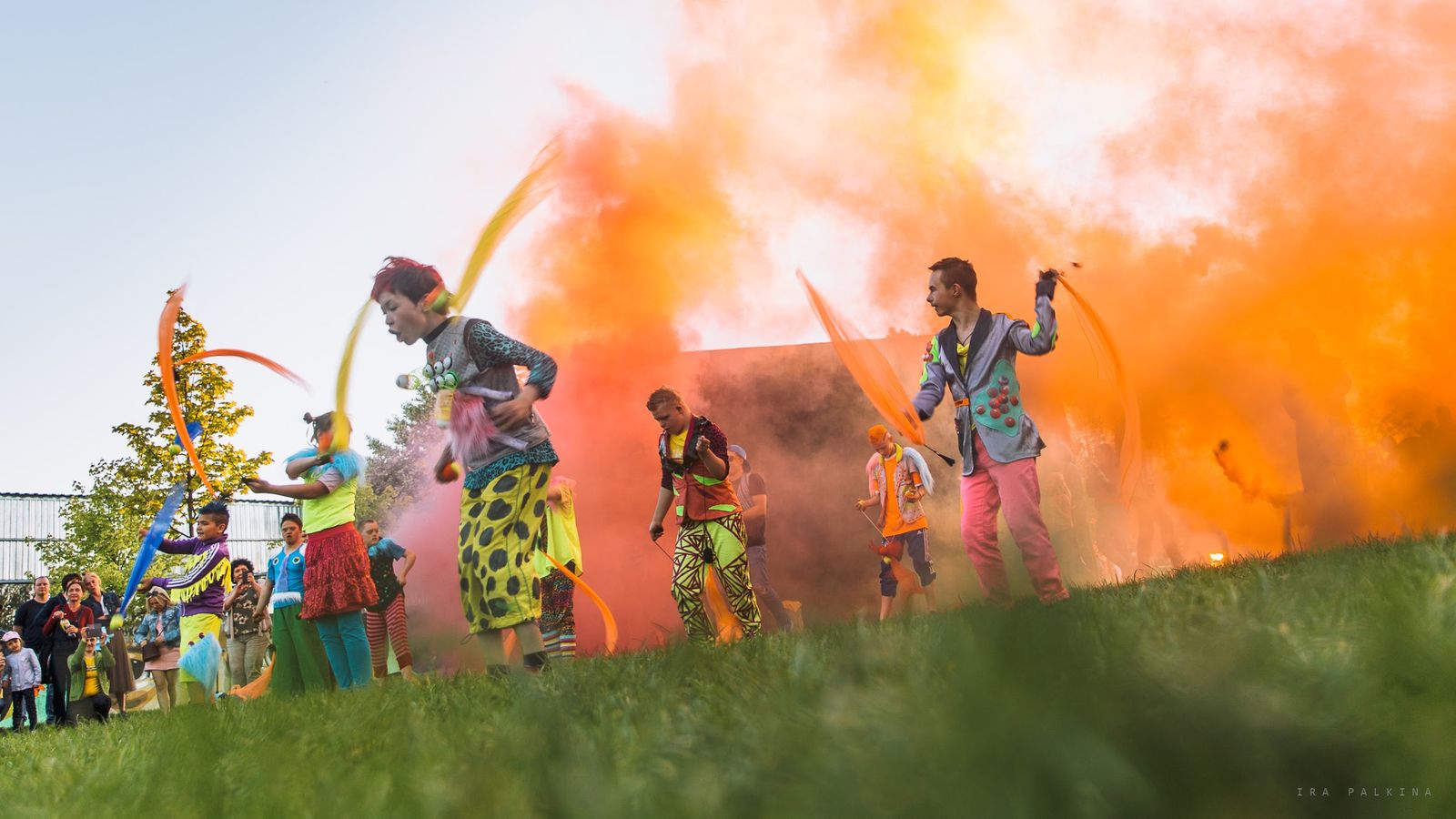 Performers in bright costumes dancing with ribbons in front of orange smoke