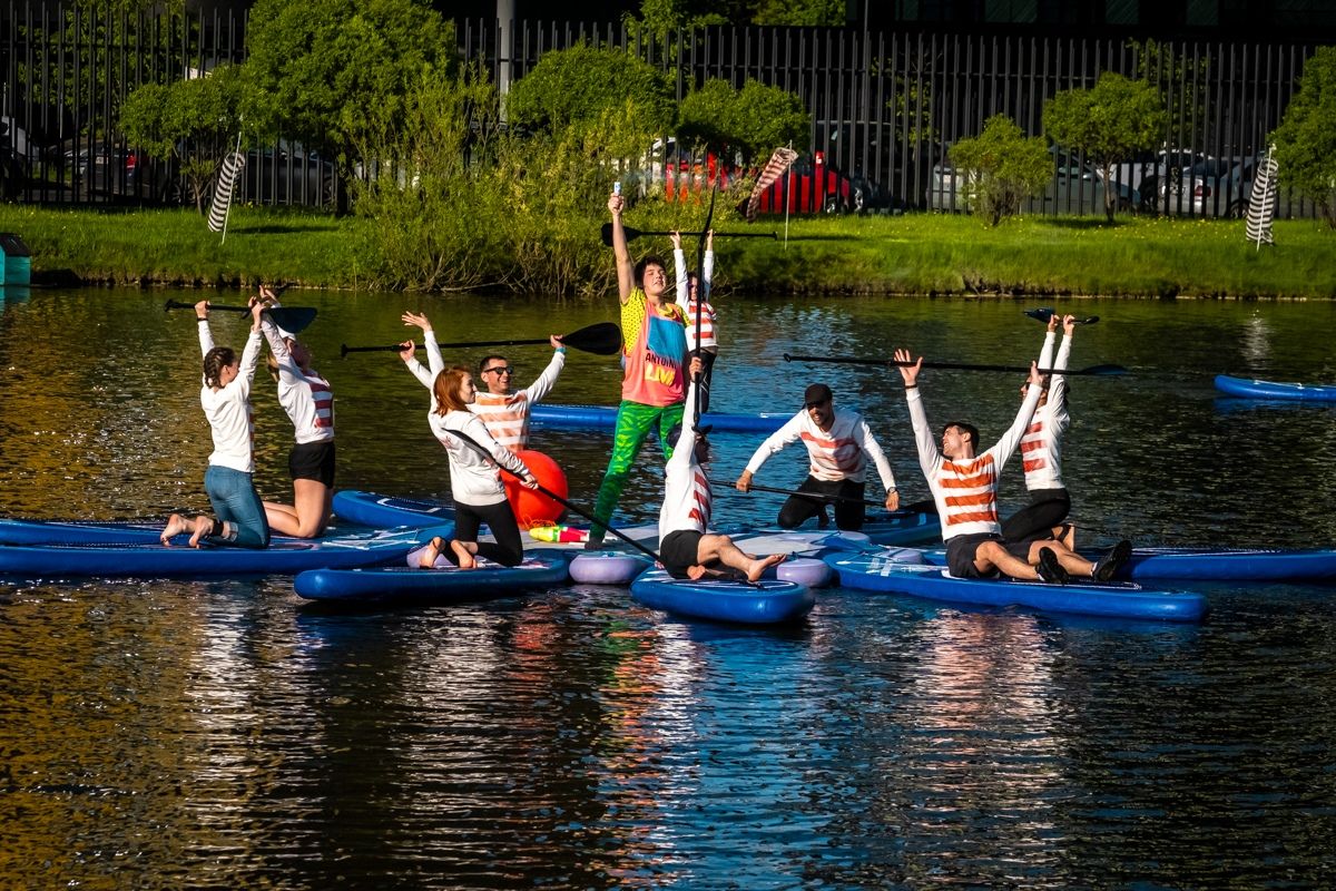 A row of SUP surfers on boards on the pond with their arms raised