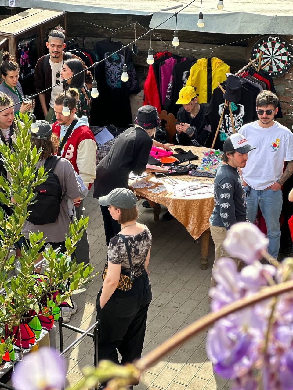 The courtyard seen from above: guests around a table of clothes under strings of bulbs, wisteria in front